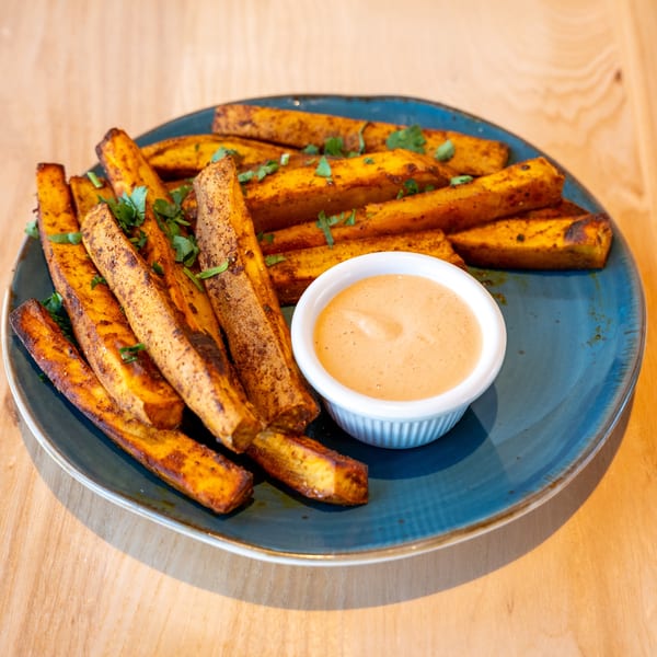 Sweet potato fries seasoned with herbs and spices, served with a side of dipping sauce on a blue plate.
