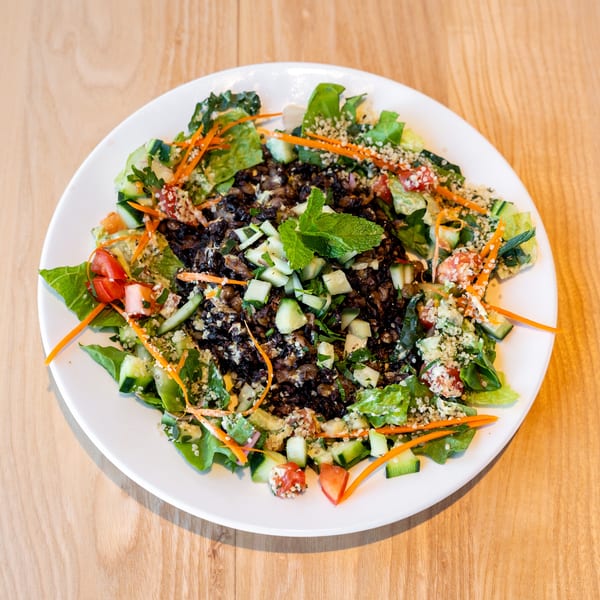 A vibrant salad with dark lentils, fresh greens, cucumbers, tomatoes, carrots, and mint on a white plate.