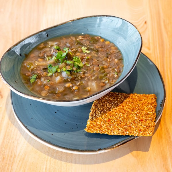 Lentil soup with fresh herbs in a blue bowl, served with a sesame seed cracker.