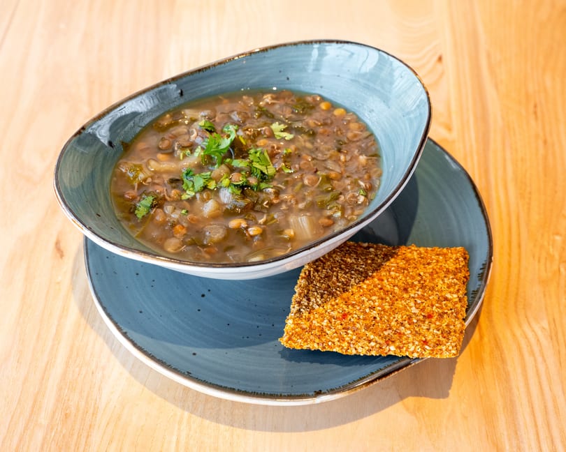 Lentil soup with fresh herbs in a blue bowl, served with a sesame seed cracker.