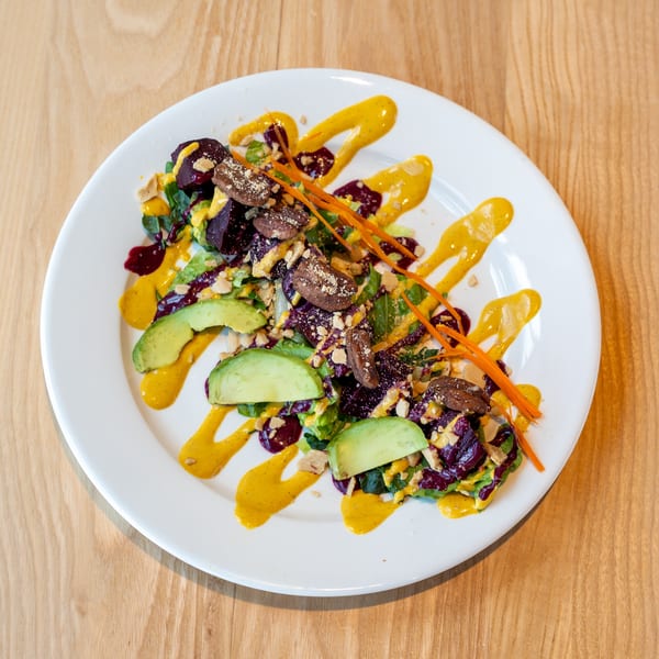 Colorful salad with beets, avocado, nuts, and orange and yellow sauces on a white plate.