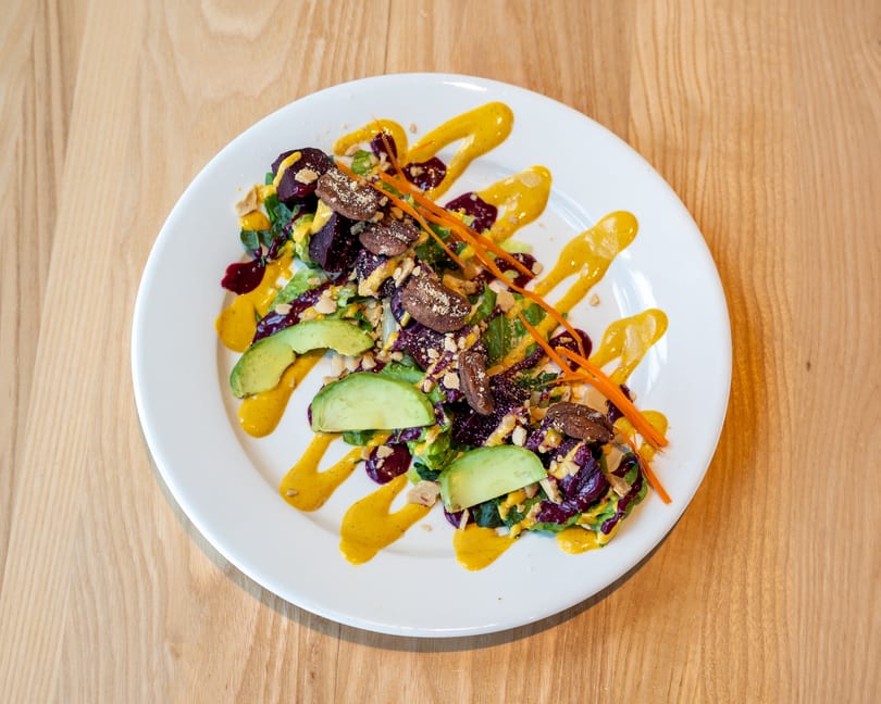 Colorful salad with beets, avocado, nuts, and orange and yellow sauces on a white plate.