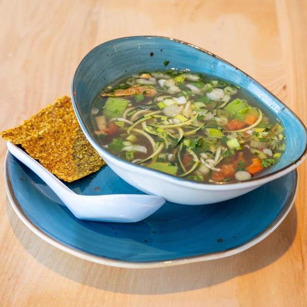 Clear vegetable soup with zucchini noodles, carrots, and scallions, served with a cracker.