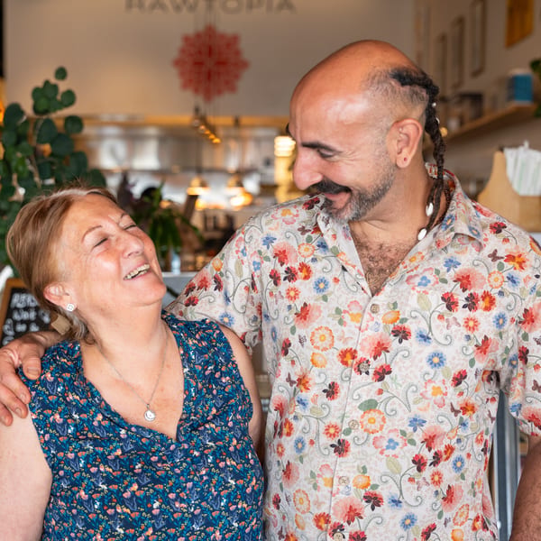 A man in a floral shirt with his arm around a laughing woman in a blue floral dress.