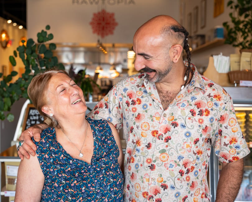 A man in a floral shirt with his arm around a laughing woman in a blue floral dress.